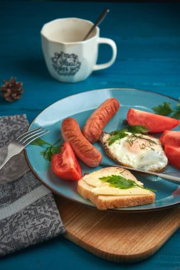 Mavi tabakta sosis ve domatesli omlet ve ahşap masa.