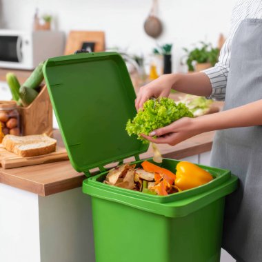 Konforlu bir apartman mutfağında, sebze artıklarını ve kabuklarını yeşil bir gübre konteynırına atar. Erdemli bir yemek hazırlarken taze malzemeler yakınlarda duruyor..