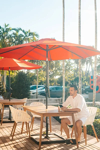 Young man in white shirt working on laptop in outdoor cafe. High quality photo