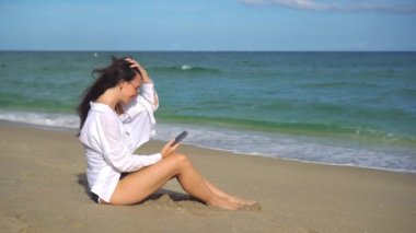 Sahilde cep telefonu kullanan genç bir kadın.