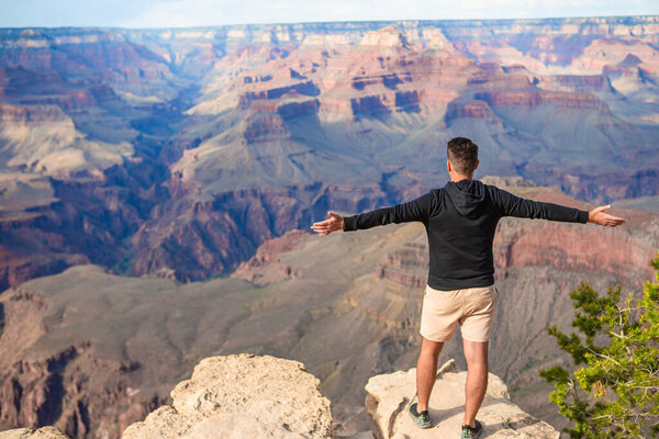 Молодой турист стоит на крутой скале, любуясь потрясающим видом на знаменитый Гранд-Каньон в прекрасный солнечный день с голубым небом летом, Национальный парк, Аризона. Высокое качество фото