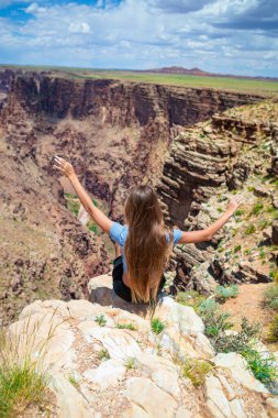 Dik bir yamaçta genç bir kız yazın güneşli bir günde Arizona 'daki Grand Canyon Ulusal Parkı' nda ünlü Büyük Kanyon 'un muhteşem manzarasını seyrediyor. Yüksek kalite fotoğraf