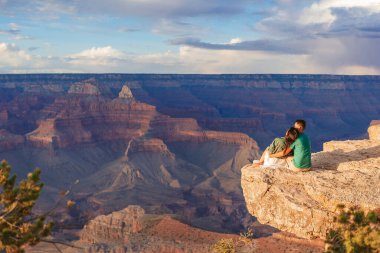 Dik bir uçurumda genç bir çift yazın güzel gün batımında muhteşem Büyük Kanyon manzarasını seyrediyor, Arizona Grand Canyon Ulusal Parkı 'nda. Yüksek kalite fotoğraf