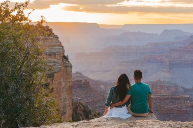 Dik bir uçurumda genç bir çift yazın güzel gün batımında muhteşem Büyük Kanyon manzarasını seyrediyor, Arizona Grand Canyon Ulusal Parkı 'nda. Yüksek kalite fotoğraf