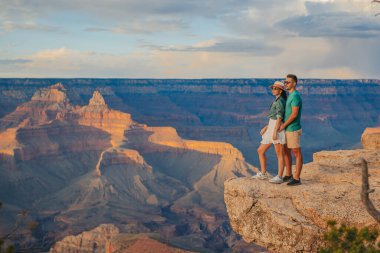 Dik bir uçurumda genç bir çift yazın güzel gün batımında muhteşem Büyük Kanyon manzarasını seyrediyor, Arizona Grand Canyon Ulusal Parkı 'nda. Yüksek kalite fotoğraf