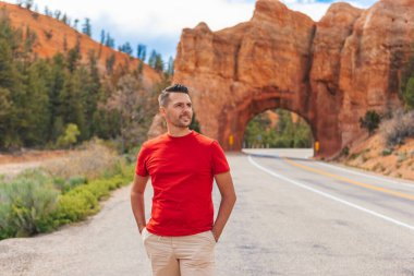 Utah, ABD 'deki Red Canyon Ulusal Parkı' ndaki doğal taş kemer köprüsünün arka planındaki genç beyaz adam.