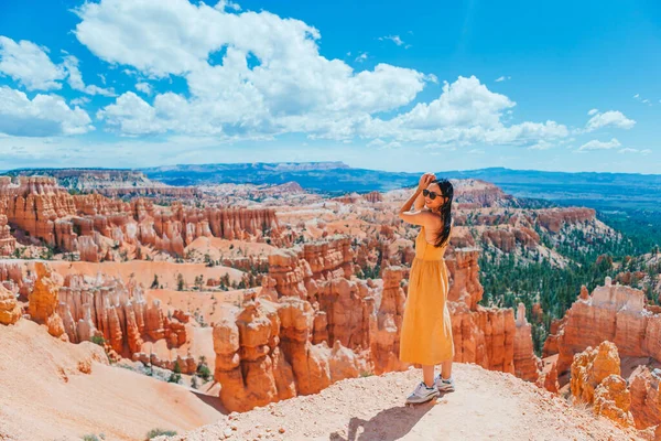Happy woman in yellow dress on trail in beautiful nature landscape with hoodoos, pinnacles and spires rock formations in Bryce Canyon National Park,Utah