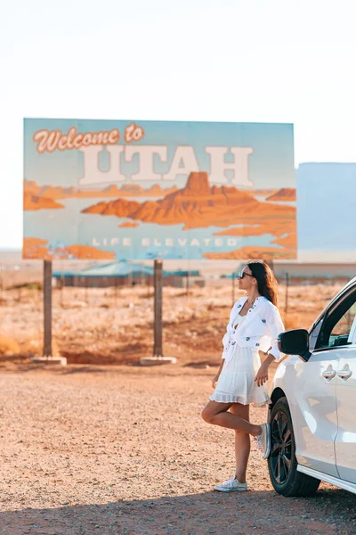 Güzel bir kadın, Utah eyalet sınırına hoş geldiniz tabelasının hemen arkasında, Anıt Vadisi 'ndeki arabanın yanında. Utah yol tabelasına hoş geldiniz..