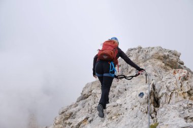 Aktif kadın ferrata kablosuyla korunuyor. Sis ile çevrili bir sırtta Tofana di Mezzo, Dolomites, İtalya 'ya doğru ilerliyor. Macera, cesaret, Avrupa, Yaz, etkinlik.