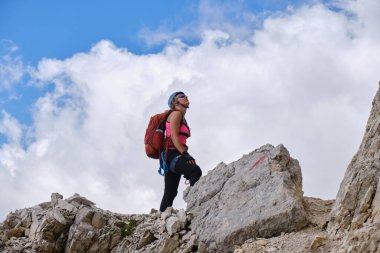 Alp tırmanma ekipmanlı bir kadın, arka planda beyaz bulutlara karşı Tofana di Mezzo, Dolomites dağlarındaki ferrata rotasına bakıyor. Yaz, aktif, turizm, Avrupa.