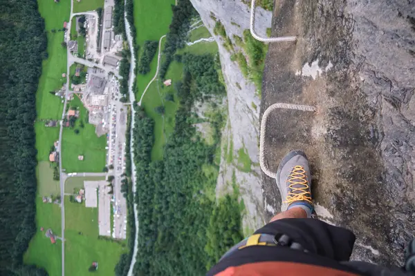 游客通过费拉塔的支架 在岩石墙的边缘行走在金属上 在他下面有巨大的垂直缝隙 可以看到下面的山谷 瑞士Murren Gimmelwald Klettersteig夏季活动 图库照片