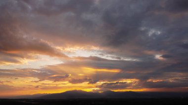Güneşin altın ışıklarıyla gün batımı gökyüzü arkadaki dağ manzaraları ve kırsal köylerin siluetlerine karşı. Gün batımında bulutlu ve güneşli güzel gökyüzü manzarası.
