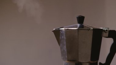Sıcak kahve kaynıyor ve moka demliğinden buhar çıkıyor, yakın plan. Gri arkaplanda kahve makinesinde kaynamış kahve. Bir çaydanlıkla nefis kahve yapmak..