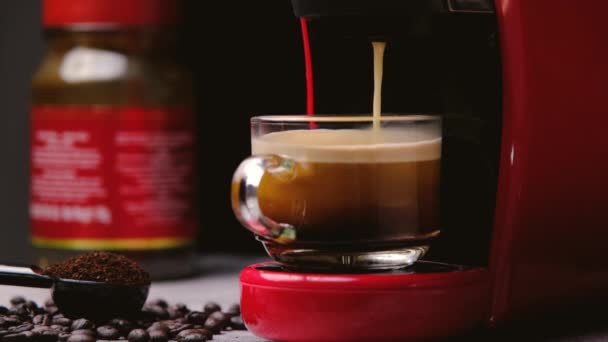 热咖啡倒入一个装有浓缩咖啡机的杯子里 这是特写 现代的咖啡机 勺子里有磨碎的咖啡 咖啡豆洒在木桌上 — 图库视频影像