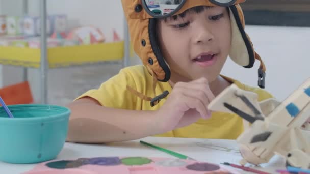 一个快乐的亚洲女孩的画像 她在教室里的一架木制玩具飞机上画了一幅画笔 儿童的艺术和手工艺 有创意的小艺术家 — 图库视频影像
