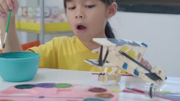 一个快乐的亚洲女孩的画像 她在教室里的一架木制玩具飞机上画了一幅画笔 儿童的艺术和手工艺 有创意的小艺术家 — 图库视频影像