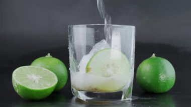 Soğuk tekilayı bardakta karıştırıp limon ve siyah arka planda tuz karıştırmak. Limon dilimleri ve su sıçratma ile bir bardak tekila. Alkolik içki konsepti. seçici odak.