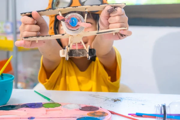教室の木製のおもちゃの飛行機にブラシの絵と幸せなアジアの女の子の肖像画 子供のための芸術品や工芸品 創作活動中の小さなアーティスト — ストック写真