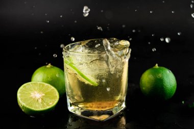 Siyah arka planda limonlu ve tuzlu altın Meksika tekilası. Limon dilimleri ve su sıçratma ile bir bardak tekila. Alkolik içki konsepti. seçici odak.