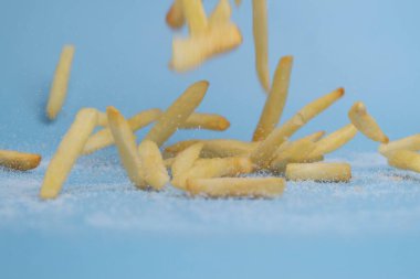 Patates kızartması ya da açık mavi arka planda tuzlu patates cipsi. Taze kızarmış patates kızartması yakın mesafede. Uçan lezzetli patates kızartması