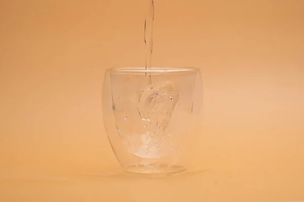 Pouring warm water into glass on vintage background. Shot of pouring water into a glass with double layer isolated on beige background.