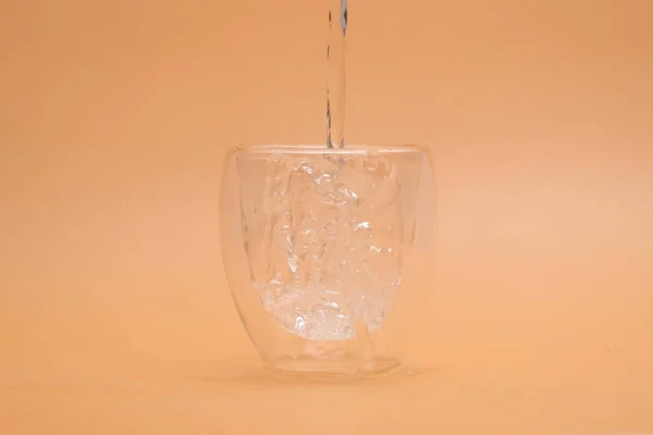 Pouring warm water into glass on vintage background. Shot of pouring water into a glass with double layer isolated on beige background.