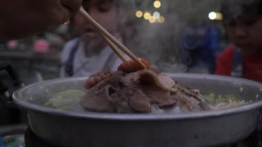 Grilled pork on the stove, Thai food buffet. Hands holding chopsticks grilling traditional Thai style BBQ with pork, prawns, beef, chicken, vegetables and soup on hot pan.