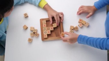 Little siblings playing wooden board game tic-tac-toe on table in living room. Family spending time together on weekend.
