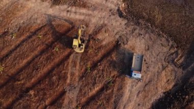Aerial view of a wheel loader excavator with a backhoe loading sand into a heavy earthmover at a construction site. Excavator digging soil pits for the agricultural industry.