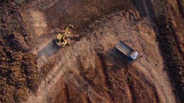 Aerial view of a wheel loader excavator with a backhoe loading sand into a heavy earthmover at a construction site. Excavator digging soil pits for the agricultural industry.