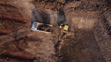Aerial view of a wheel loader excavator with a backhoe loading sand into a heavy earthmover at a construction site. Excavator digging soil pits for the agricultural industry.