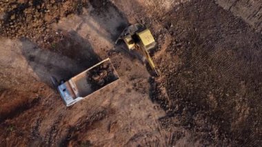 Aerial view of a wheel loader excavator with a backhoe loading sand into a heavy earthmover at a construction site. Excavator digging soil pits for the agricultural industry.