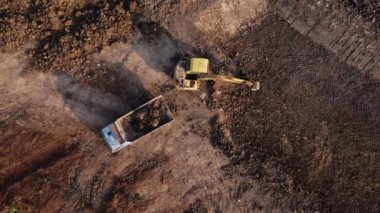 Aerial view of a wheel loader excavator with a backhoe loading sand into a heavy earthmover at a construction site. Excavator digging soil pits for the agricultural industry.