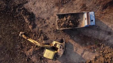 Aerial view of a wheel loader excavator with a backhoe loading sand into a heavy earthmover at a construction site. Excavator digging soil pits for the agricultural industry.