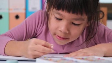 Kağıt üzerinde pastel boyayla çizen mutlu küçük kız evdeki masasında oturuyor. İnce motor becerilerin yaratıcılığı ve gelişimi.