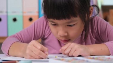 Happy little girl drawing with crayon on paper sitting at table in her room at home. Creativity and development of fine motor skills.