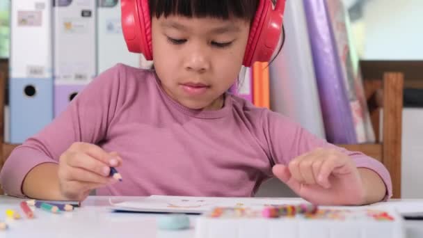 Fröhliches Kleines Mädchen Mit Kopfhörern Das Mit Buntstiften Auf Papier — Stockvideo