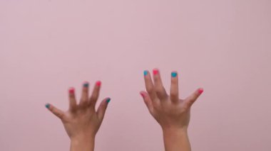 Tırnak cilasını gösteren ve stüdyodaki pastel pembe arka planda el sallayan çocuk elinin yakın çekimi. Hareket ve vücut dili paketi.