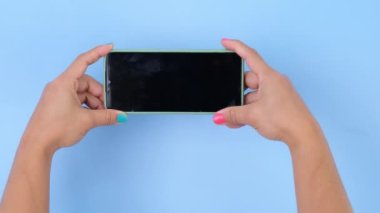 Stüdyoda pastel mavi arka planda akıllı telefonu tutan bir kadın. Yakın plan kadın el telefonu ile Swiping, Scrolling, Daktilo veya İzleme içeriği için akıllı telefon kullan.