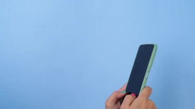 Stüdyoda pastel mavi arka planda akıllı telefonu tutan bir kadın. Yakın plan kadın el telefonu ile Swiping, Scrolling, Daktilo veya İzleme içeriği için akıllı telefon kullan.