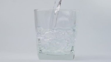Beyaz arka planda izole edilmiş bardağa saf içme suyu dökülüyor. Yakından şişeden cama su dökülüyor..