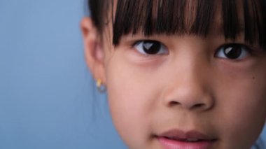 Sevimli küçük kız, elleri mavi arka planda komik bir surat yapıyor..