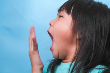 Ağzı kötü kokan Asyalı bir kız. Çocuk kız elleriyle nefesini kontrol ediyor. Oral sağlık sorunları veya diş bakımı kavramı.
