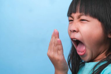 Ağzı kötü kokan Asyalı bir kız. Çocuk kız elleriyle nefesini kontrol ediyor. Oral sağlık sorunları veya diş bakımı kavramı.