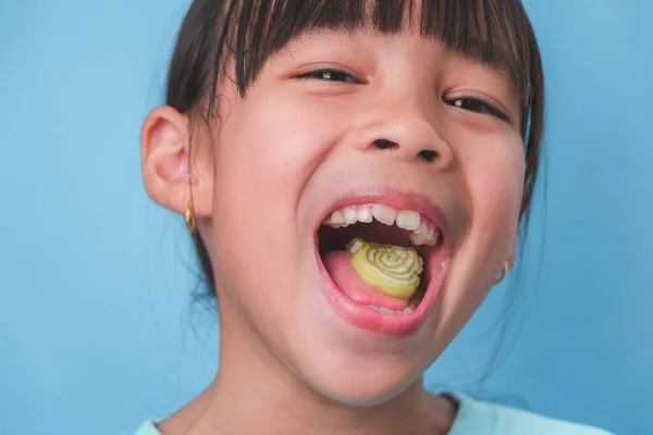 stock image Smiling cute little girl eating sweet gelatin with sugar added isolated on blue background. Children eat sugary sweets, causing loss teeth or tooth decay and unhealthy oral care.