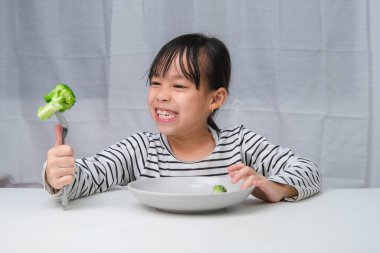 Çocuklar sebze yemeyi severler. Yemekte sağlıklı sebze yiyen tatlı Asyalı kız. Çocuklar için beslenme ve sağlıklı yeme alışkanlıkları.