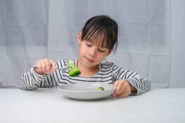 Çocuklar sebze yemeyi severler. Yemekte sağlıklı sebze yiyen tatlı Asyalı kız. Çocuklar için beslenme ve sağlıklı yeme alışkanlıkları.