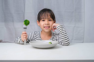 Çocuklar sebze yemeyi severler. Yemekte sağlıklı sebze yiyen tatlı Asyalı kız. Çocuklar için beslenme ve sağlıklı yeme alışkanlıkları.