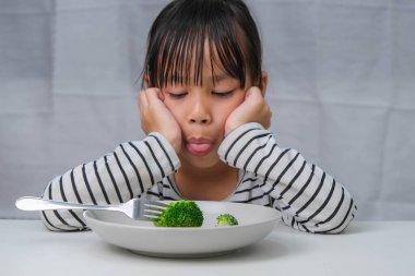Çocuklar sebze yemeyi sevmez. Sağlıklı sebze yemeyi reddeden sevimli Asyalı kız. Çocuklar için beslenme ve sağlıklı yeme alışkanlıkları.