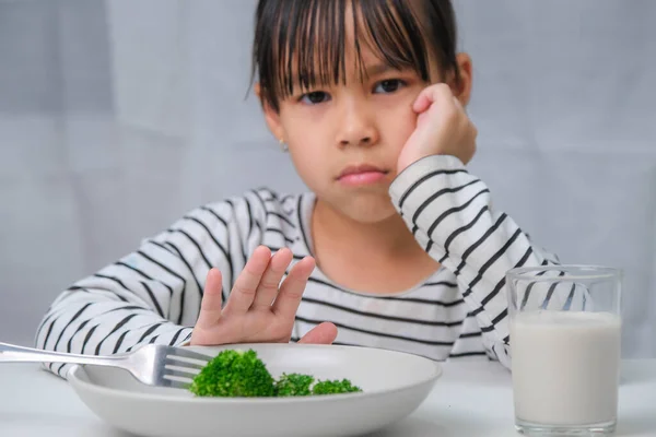 Children don\'t like to eat vegetables. Cute Asian girl refusing to eat healthy vegetables. Nutrition and healthy eating habits for children.